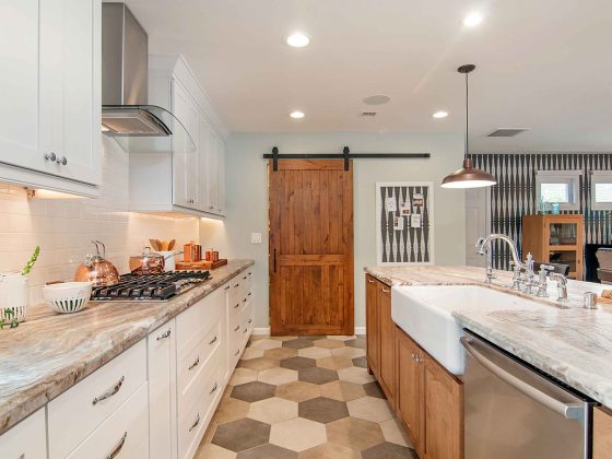 An open-space concept, galley kitchen with light paint colors and stainless steel appliances. The pantry has a custom barn door.