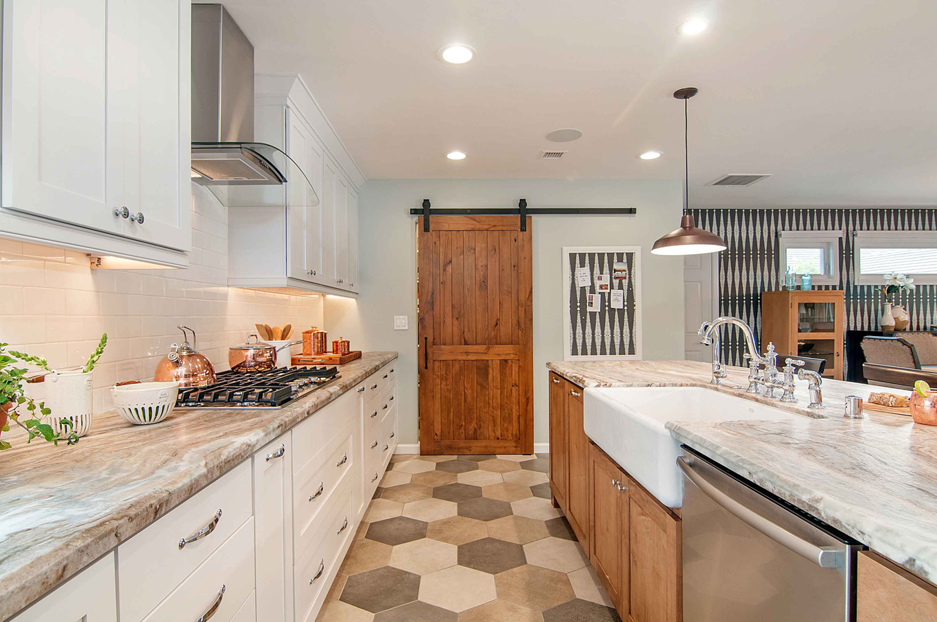 An open-space concept, galley kitchen with light paint colors and stainless steel appliances. The pantry has a custom barn door.