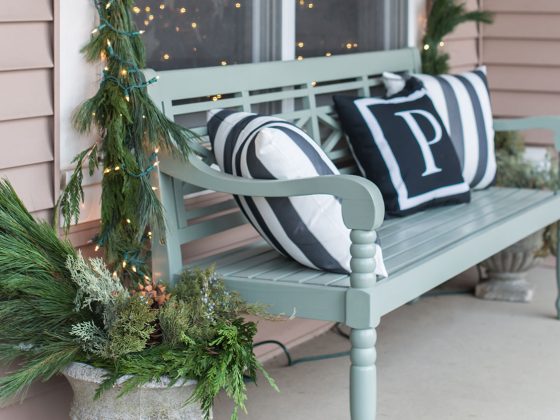 Fresh greenery Christmas decor with a garland around a window and a blue bench on the porch