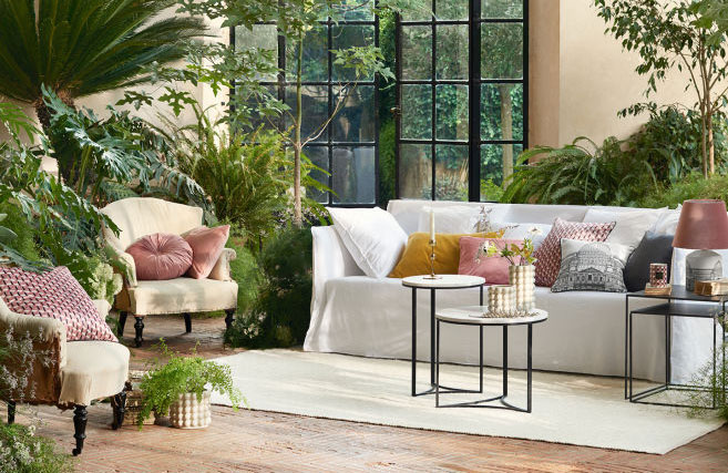 living room with lots of house plants and colorful pillows on a white slipcovered sofa