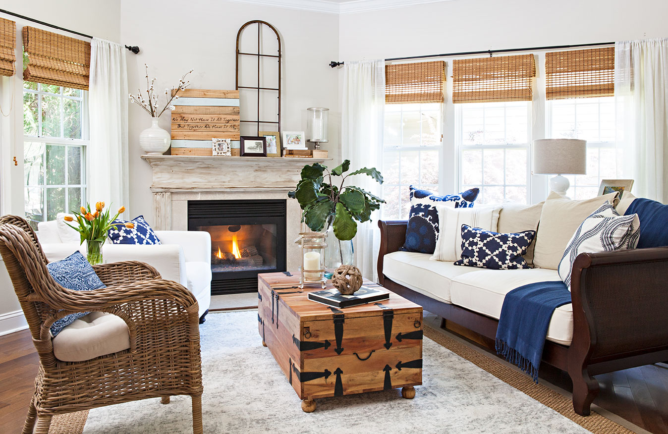 Spacious living room with light gray/beige walls, wicker and wooden rustic furniture accent pieces and pops of blue in pillows and throws.