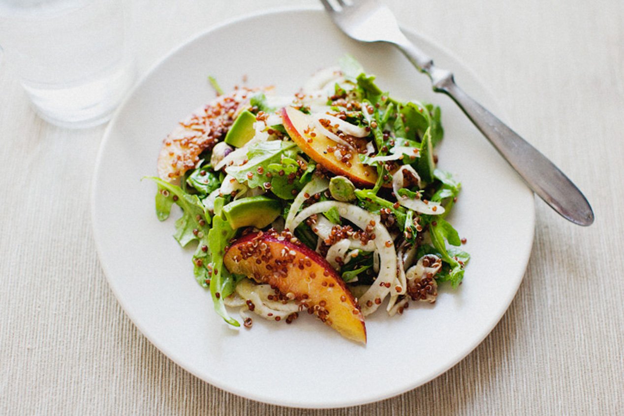 Perfectly plated nectarine and avocado salad on a white plate with a silver fork balancing on the edge.