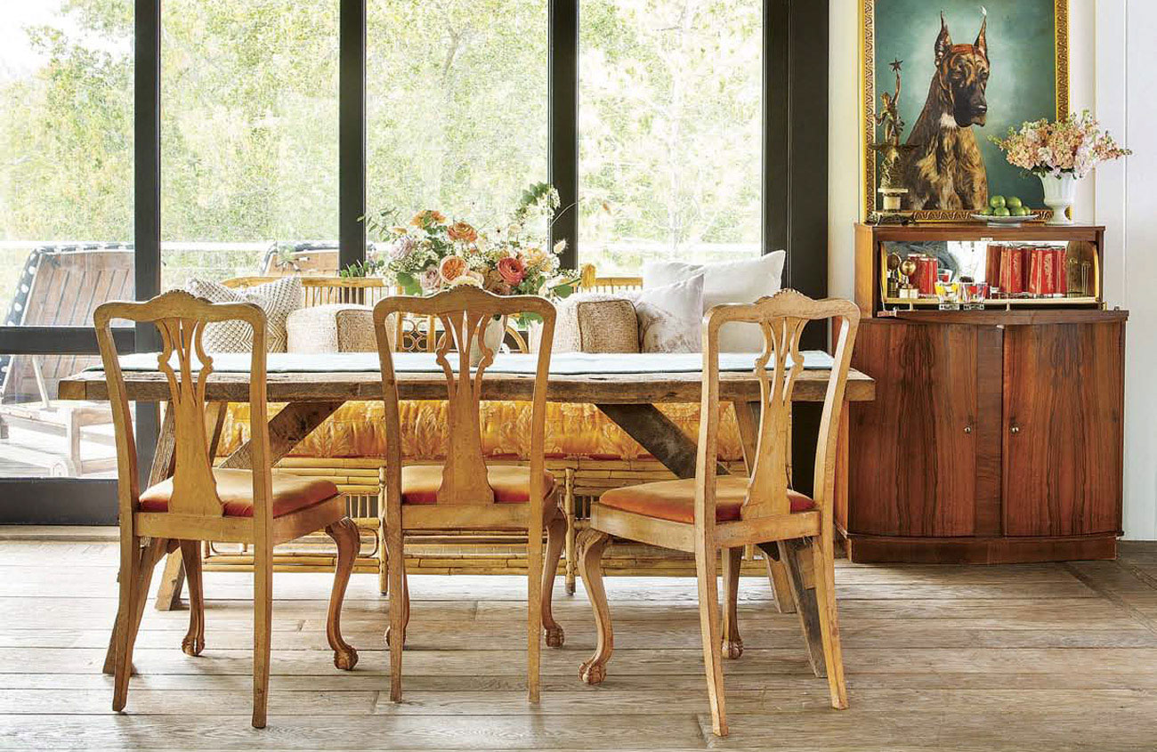 Handmade wooden dining table surrounded by intricate dining chairs, looking out a large wall of windows next to a fold down bar.