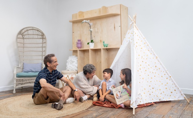 A couple plays with two small children with a tent in a playroom.