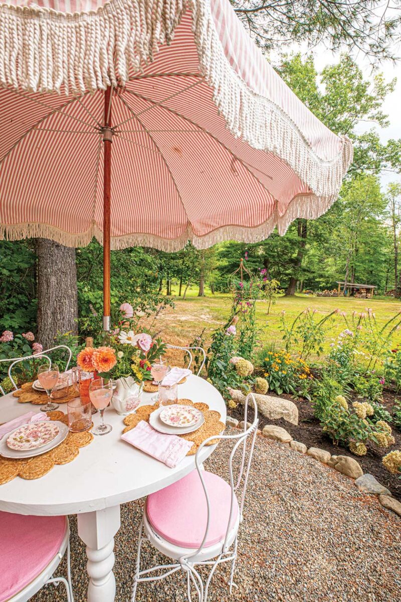 fringed pink and white umbrella and pink and white bistro chairs in outdoor dining area